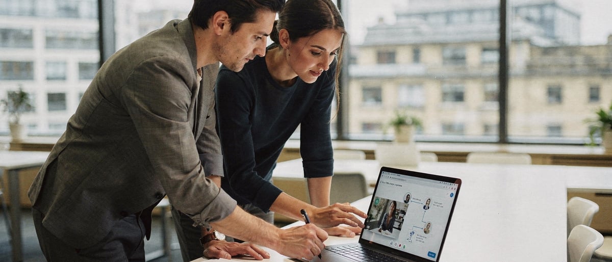 Two marketing colleagues in a bright London office clicking through an interactive video on a laptop while sketching a customer journey on a notepad