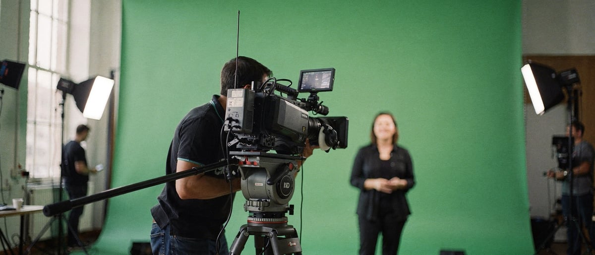 Presenter checking posture at camera mark on green-screen stage while director monitors composited output