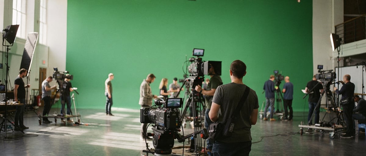 Presenter preparing in a green-screen virtual studio with warm broadcast lighting and composited background