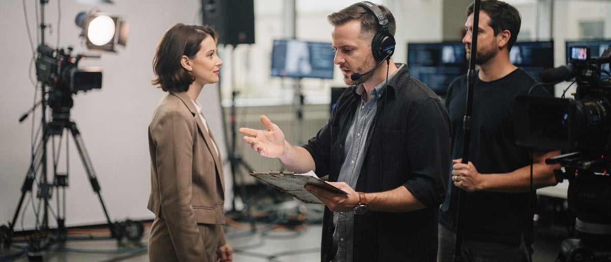 Crew member quietly coaching a presenter on a bright green-screen studio floor before take