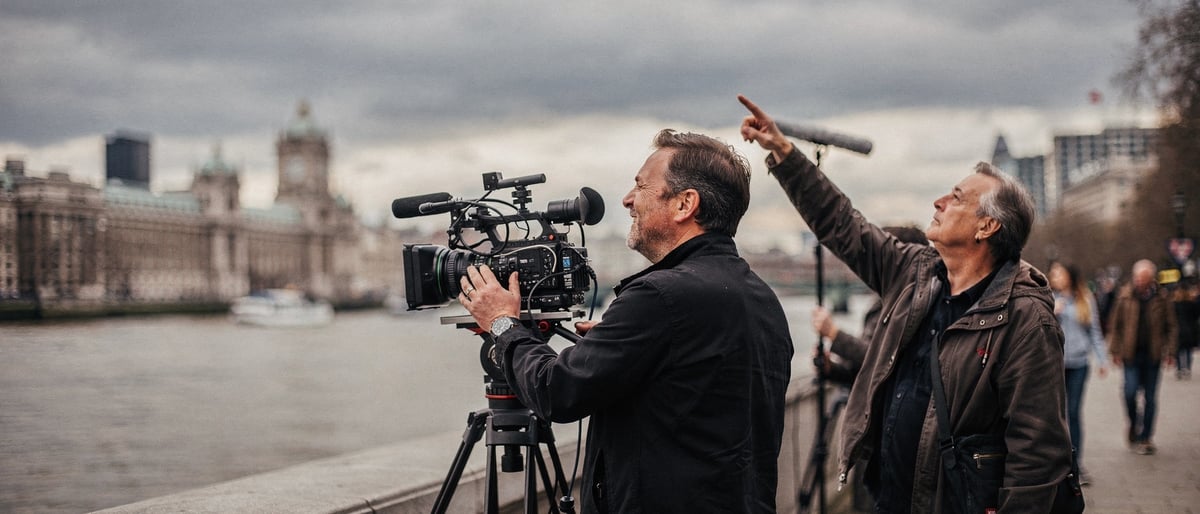 A documentary film crew filming on the South Bank promenade beside the River Thames under an overcast sky