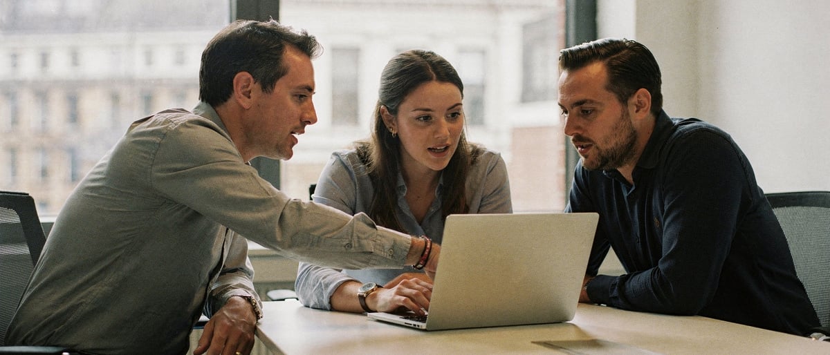 Three marketing colleagues reviewing an older brand film on a laptop in a bright London meeting room