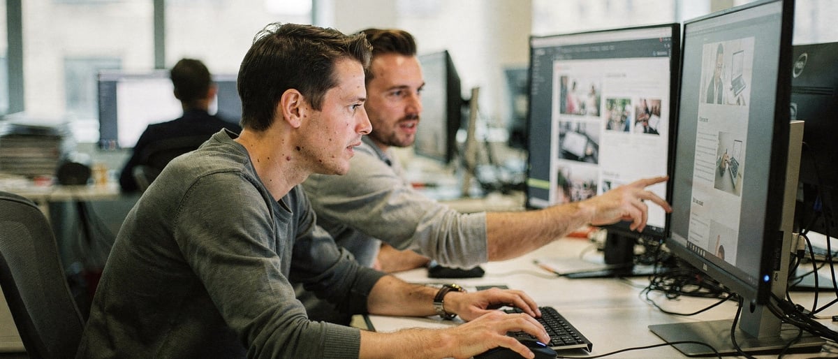 Two web editors reviewing a website layout across several monitors in a bright modern London office