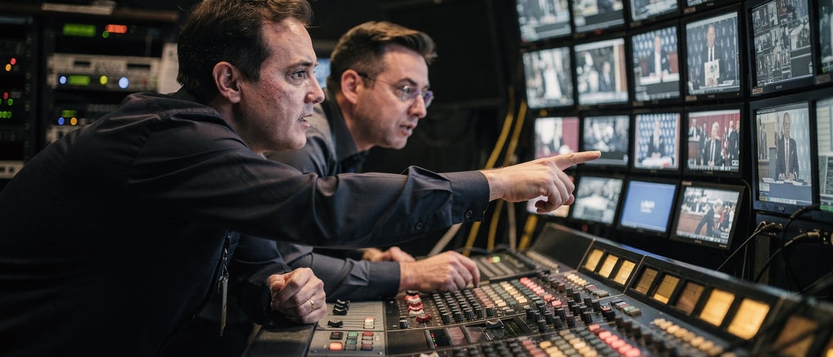 Two broadcast engineers at a vision-mixing desk in a dim control gallery switching to a backup feed during a live show