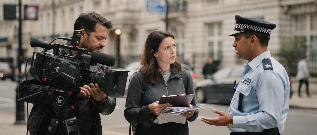 A small film crew with a tripod-mounted camera pause on a London street corner as a council officer speaks to the producer holding a clipboard