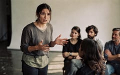 A woman speaking and gesturing to a small seated audience on a studio floor