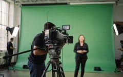 Presenter checking posture at camera mark on green-screen stage while director monitors composited output
