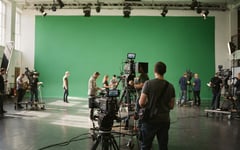 Presenter preparing in a green-screen virtual studio with warm broadcast lighting and composited background