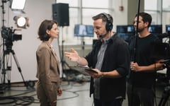 Crew member quietly coaching a presenter on a bright green-screen studio floor before take