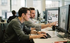 Two web editors reviewing a website layout across several monitors in a bright modern London office