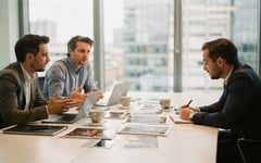 Two production company executives showing their showreel and past work to a prospective buyer across a meeting room table in a bright London office