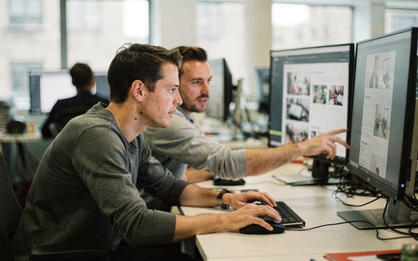 Two web editors reviewing a website layout across several monitors in a bright modern London office