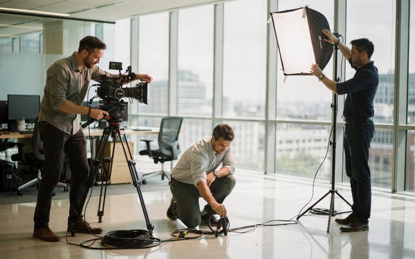 A small film crew setting up a cinema camera, lighting and cabling in a bright London office before a shoot